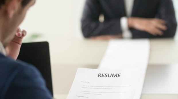 Back view of employer reading resume focus on document, job applicant waiting for hiring decision at desk on background. Hiring manager studying long list of candidates achievements and experiences
